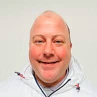 Headshot of a Caucasian man smiling. He is bald and is wearing a navy blue shirt